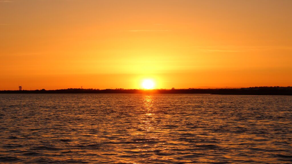 Una vibrante puesta de sol sobre el Parque Natural de Ria Formosa, con el sol cerca del horizonte, proyectando un resplandor dorado sobre el agua y el cielo.